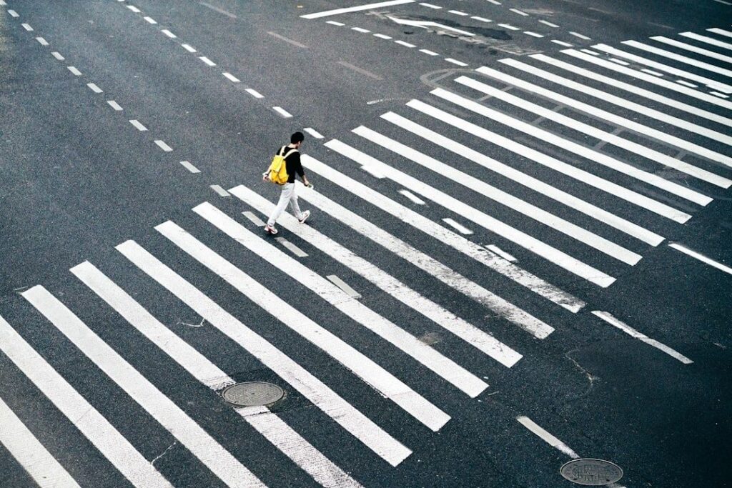 Pedestrian crossing a broad, striped urban intersection